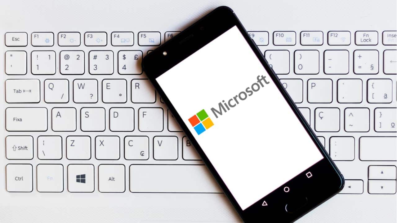 Celular sobre teclado de computador mostra logo da Microsoft na tela