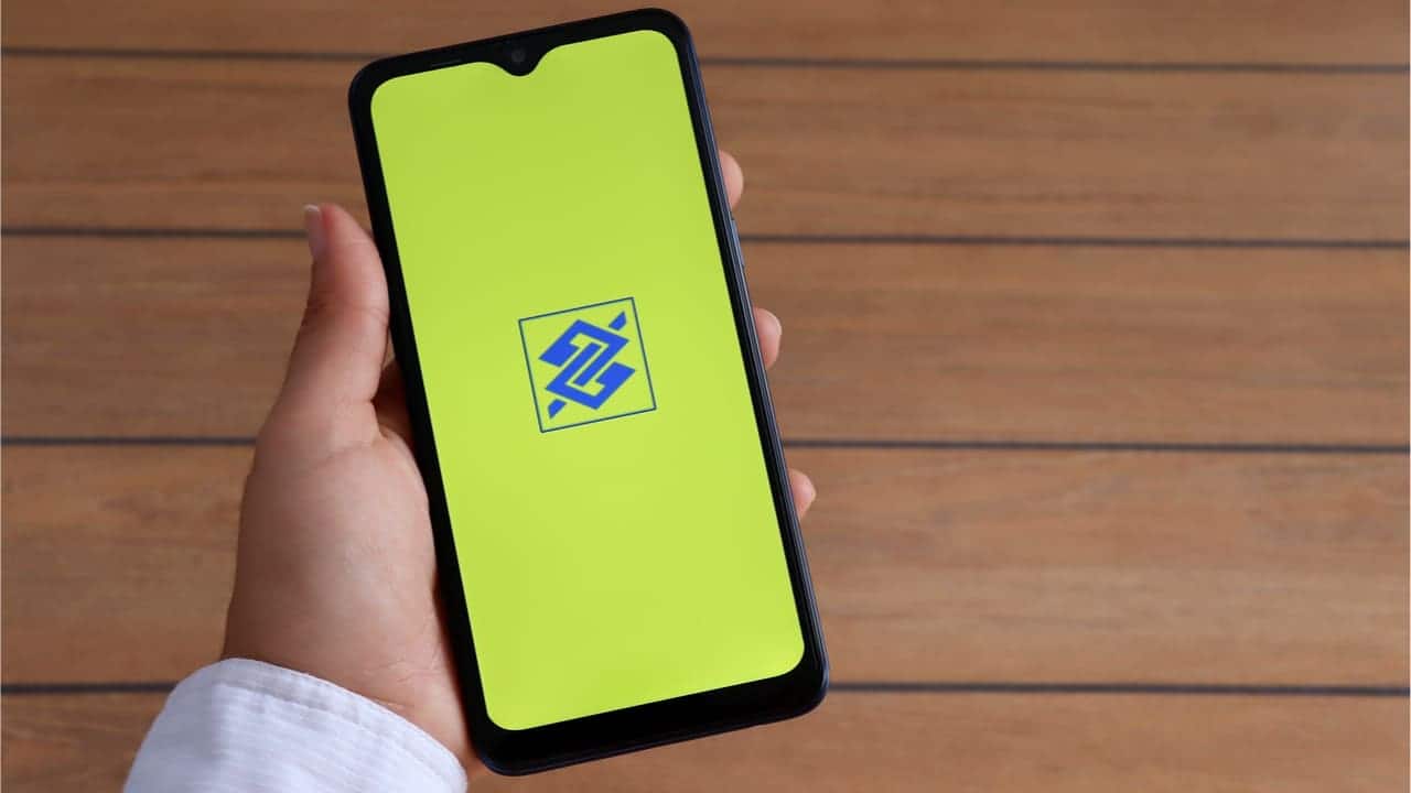 Imagem de mão segurando celular que mostra logo do Banco do Brasil