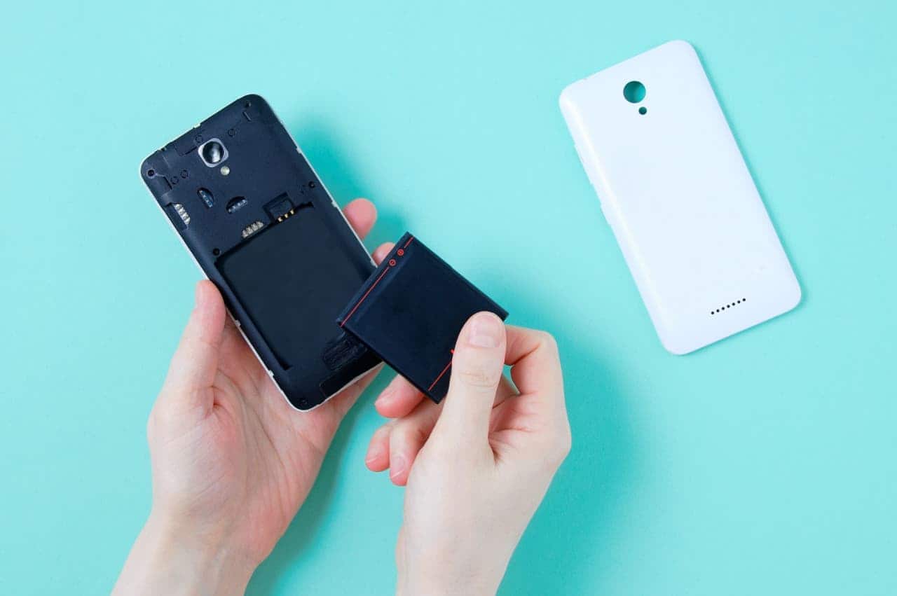 Mãos de uma pessoa retirando bateria removível de celular. Ao lado, a capa traseira do aparelho.