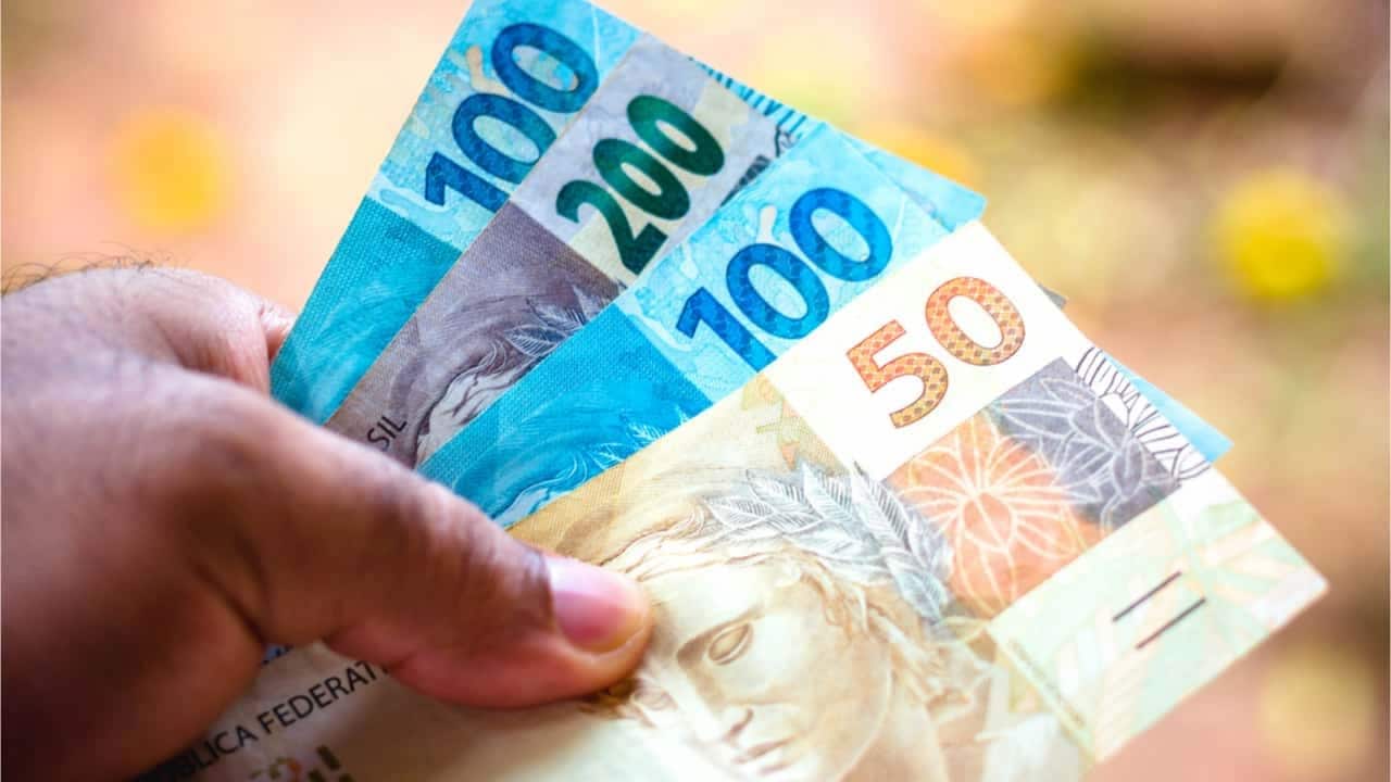 Pessoa segurando notas de 50, 100 e 200 reais
