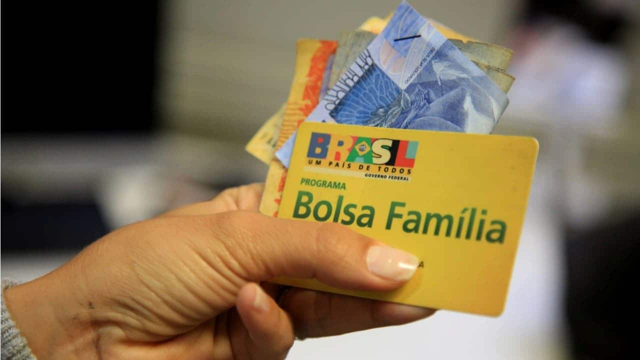 Pessoa segurando cartão do Bolsa Família e algumas cédulas de real