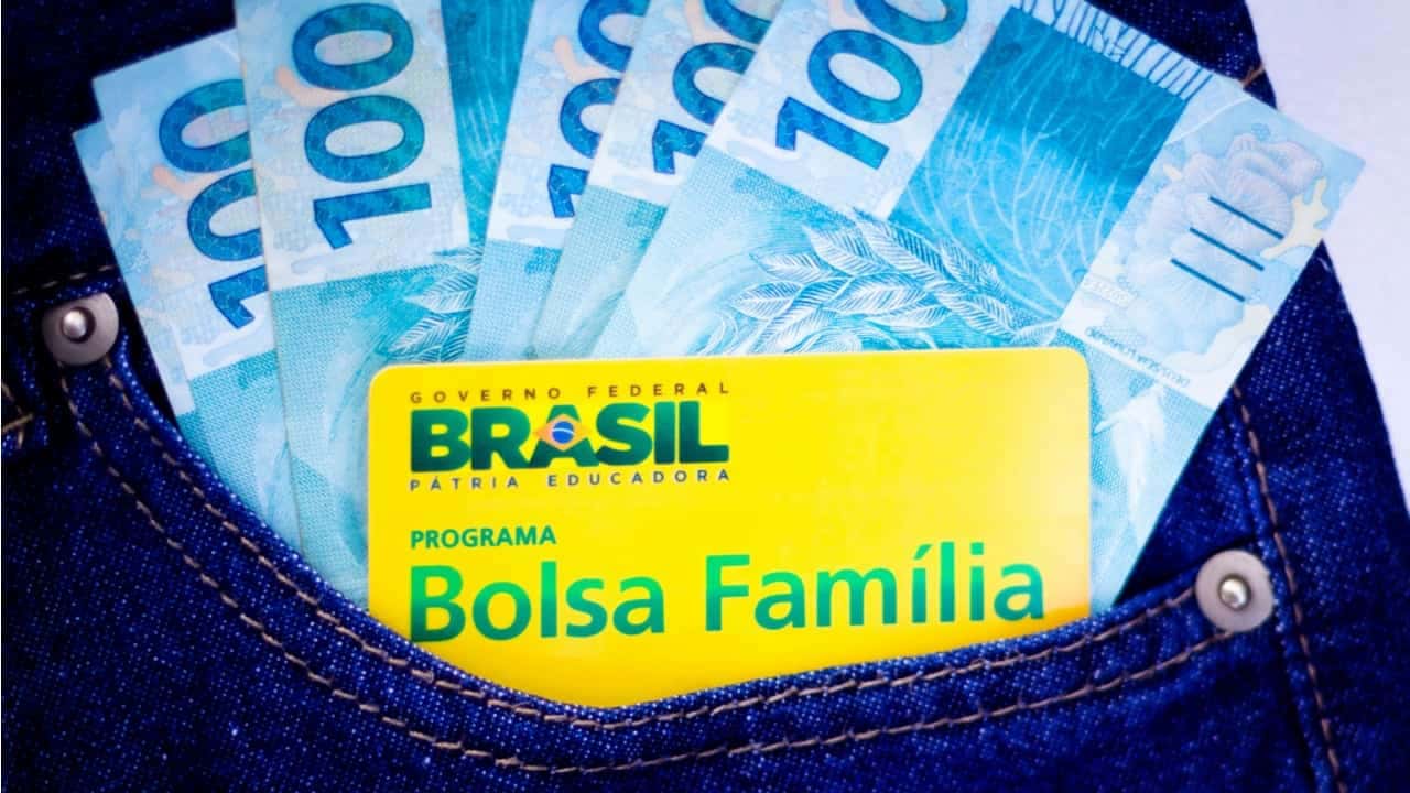 Cartão Bolsa Família e notas de 100 reais no bolso de uma roupa jeans