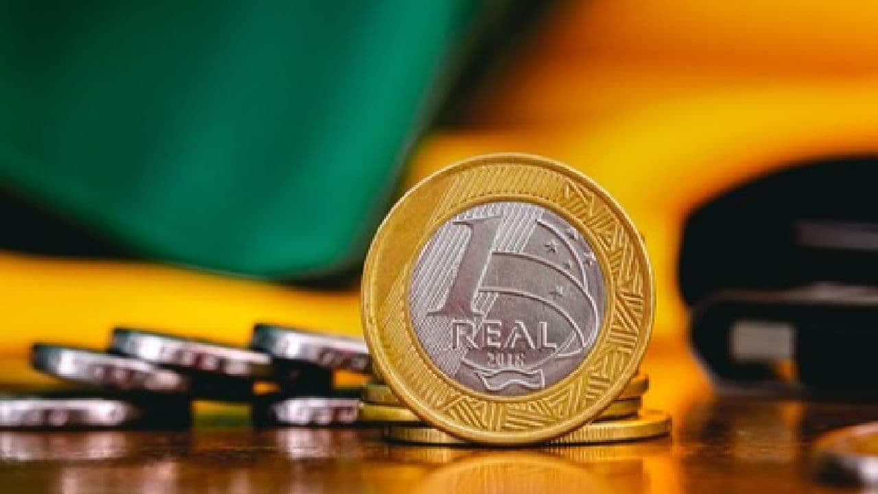 imagem de moedas de 1 real e no fundo bandeira brasileira dívida país meta fiscal