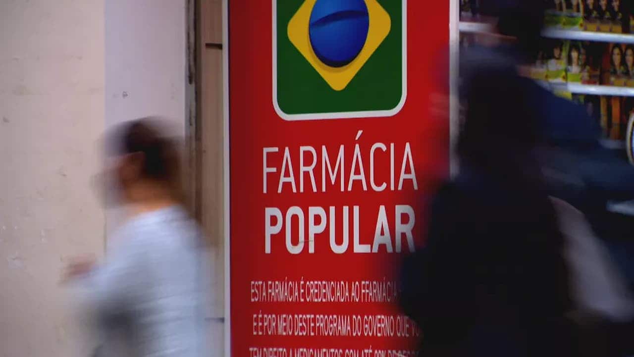 Fachada de farmácia popular com pessoas embaçadas passando pela frente
