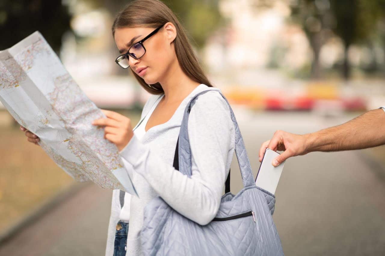 Turista distraída consultando um mapa enquanto uma mão rouba o celular de sua bolsa pelas costas