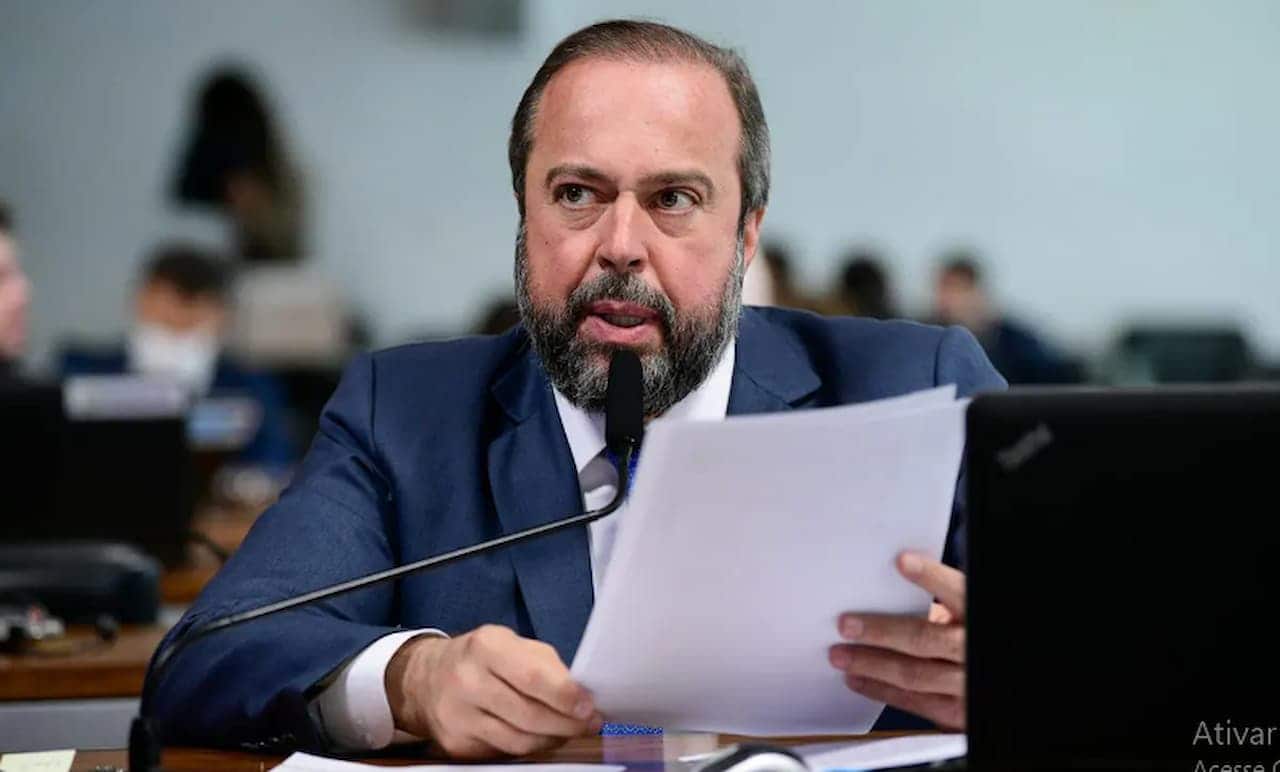 Alexandre Silveira sentado com algumas folhas de papel na mão, falando ao microfone