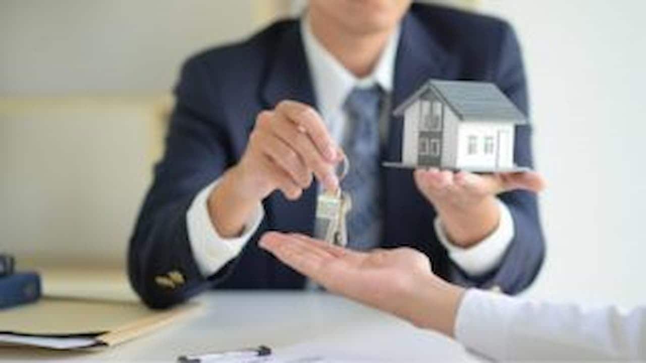 Pessoa segurando uma maquete de casa em uma mão e passando a chave da casa para outra pessoa