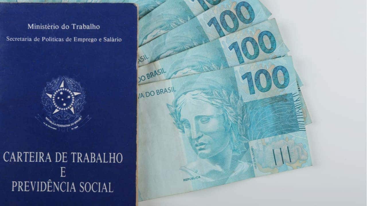 Carteira de trabalho ao lado de notas de 100 reais
