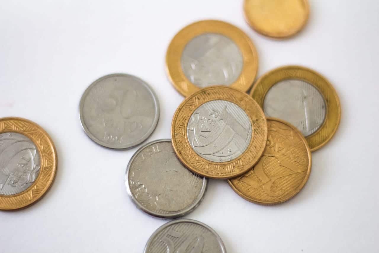 Várias moedas de um real e cinquenta centavos jogadas em cima de uma mesa.
