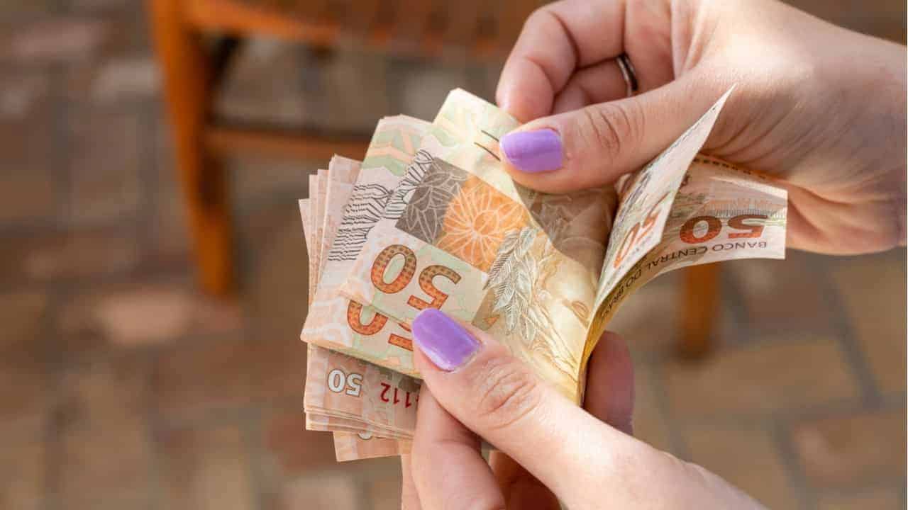 Mãos de uma pessoa contando notas de 50 reais