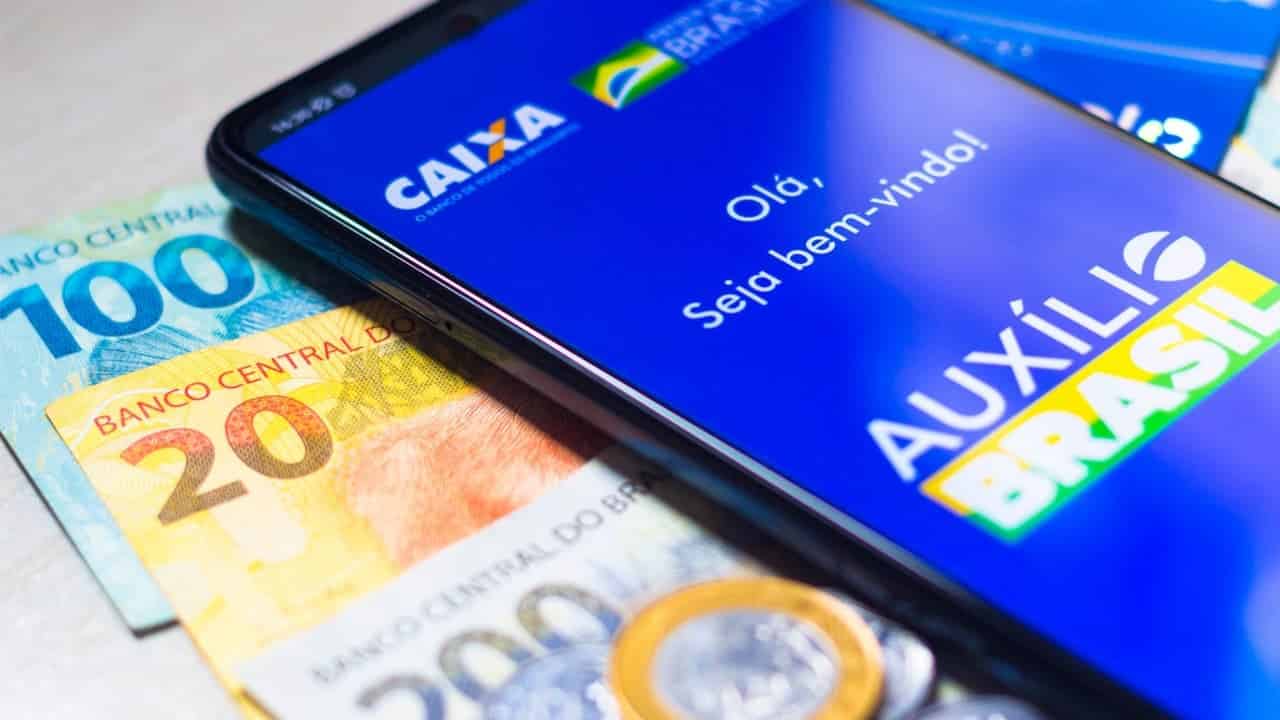 Celular mostrando tela inical do aplicativo Auxílio Brasil sobre notas de real
