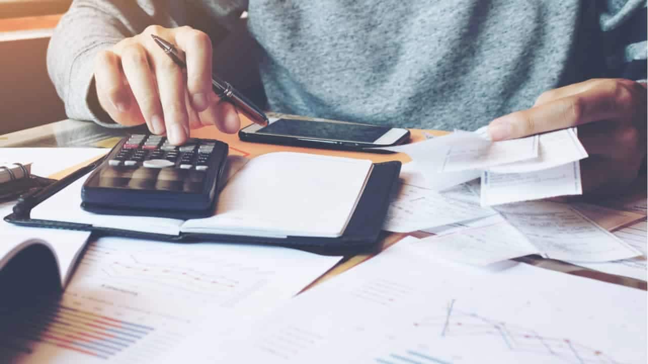 Uma pessoa realizando contas na calculadora com documentos espalhados