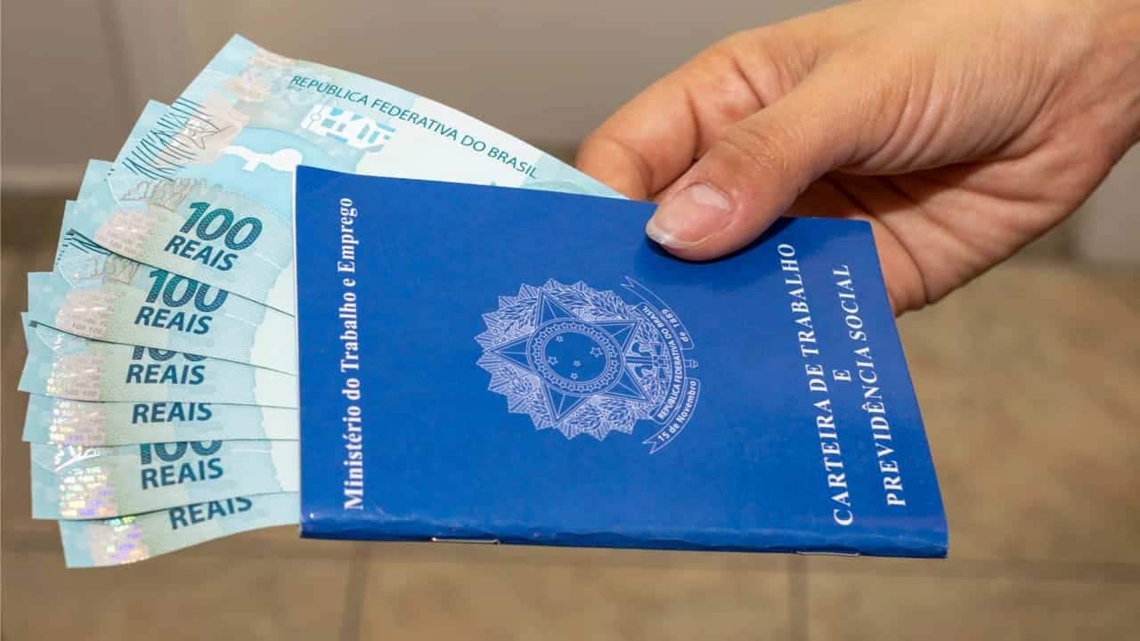 Pessoa segurando carteira de trabalho com notas de 100 reais dentro