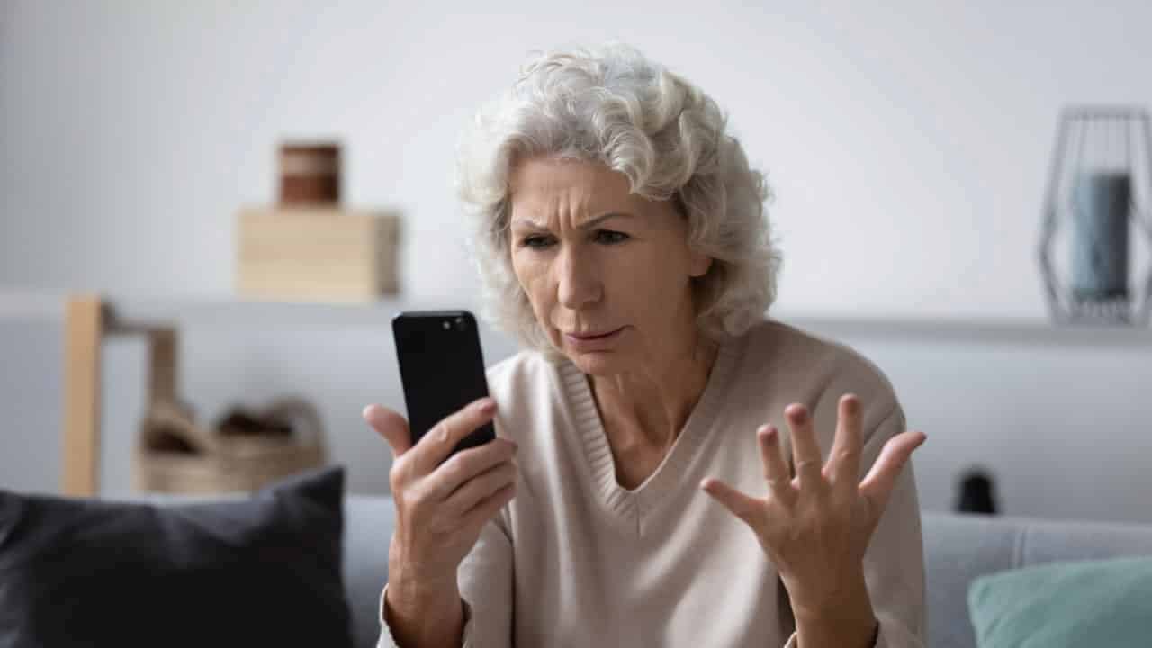 Uma mulher idosa segurando um celular com ar de surpresa