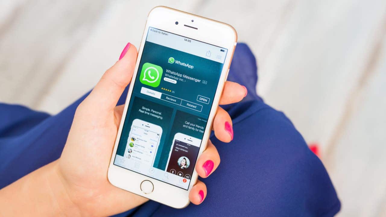 Mão feminina segurando iPhone branco que mostra tela de download do aplicativo WhatsApp
