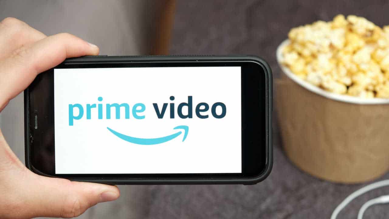 Celular na mão com aplicativo do Prime Video aberto e balde de pipoca ao fundo