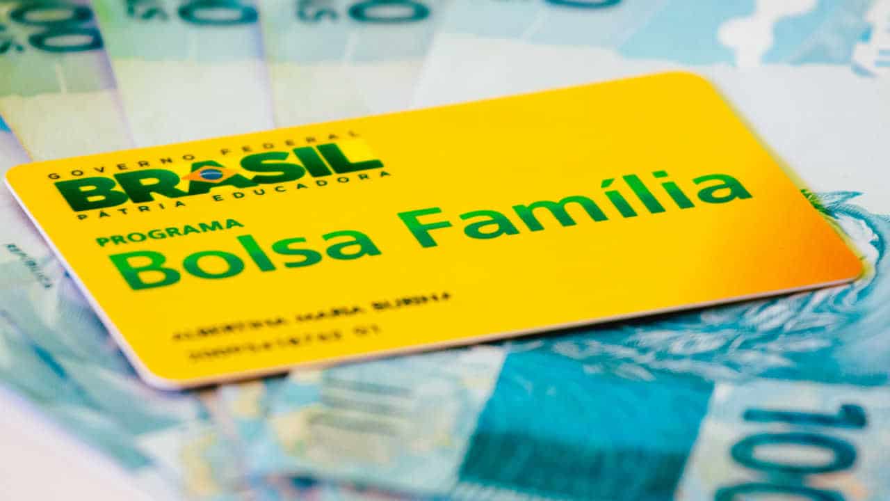 Cartão do Bolsa Família em cima de notas de R$ 100