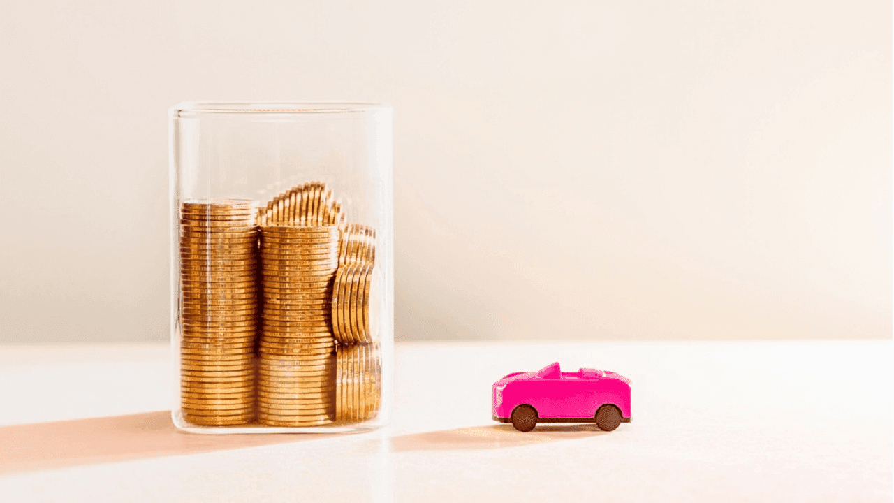 Imagem de um veículo rosa em miniatura ao lado de um pote cheio de moedas.