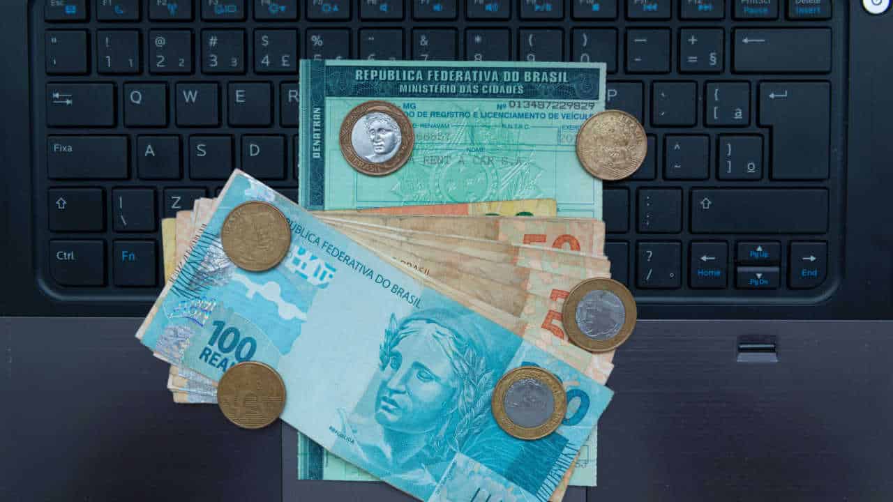 carteira de motorista, cédulas de reais e moedas sobre um teclado de computador