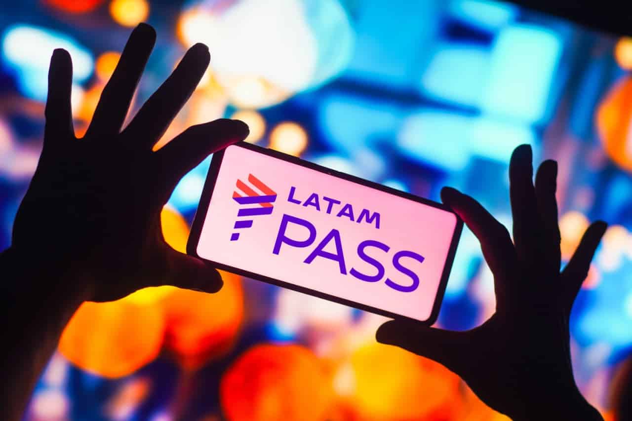 Mãos seguram smartphone cuja tela exibe o logo do LATAM Pass