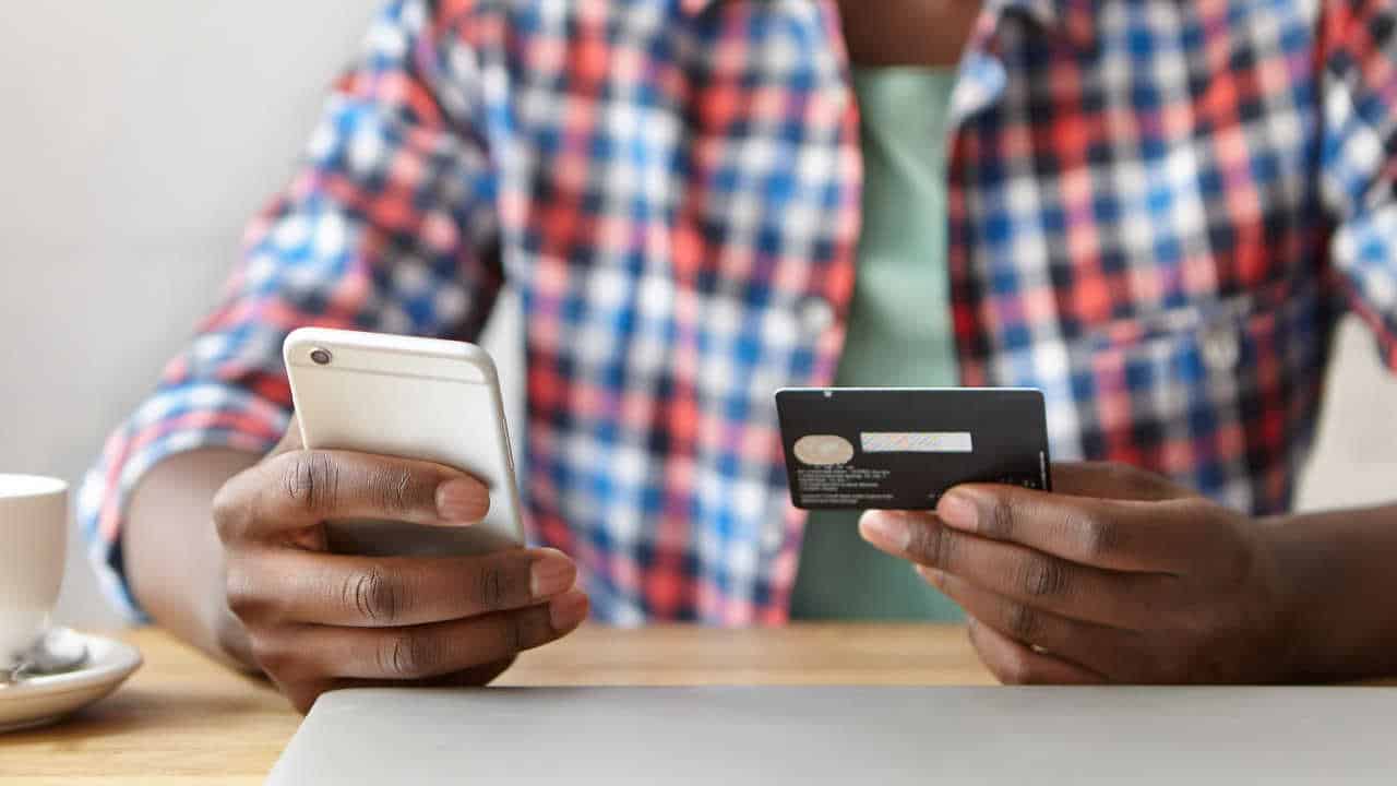 pessoa segurando o celular em uma mão e um cartão de crédito na outra mão
