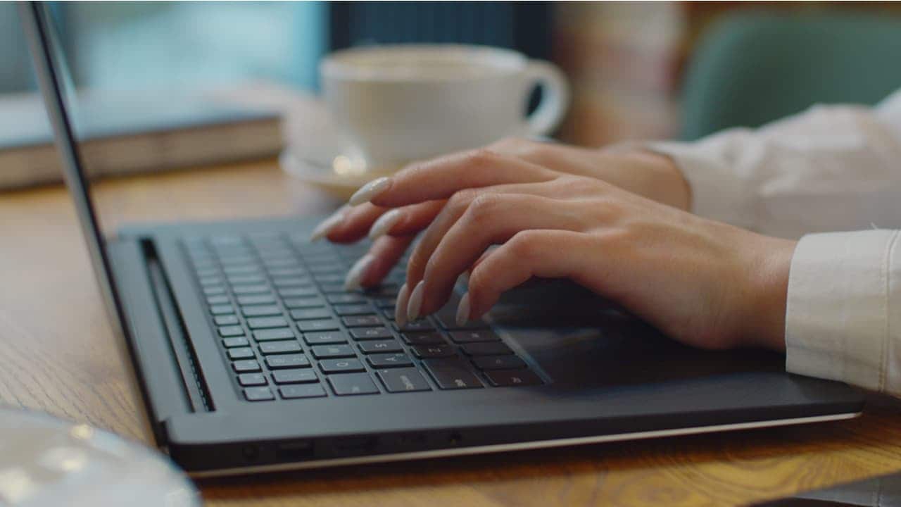 Pessoa mexendo no notebook com xícara de café ao fundo renda extra