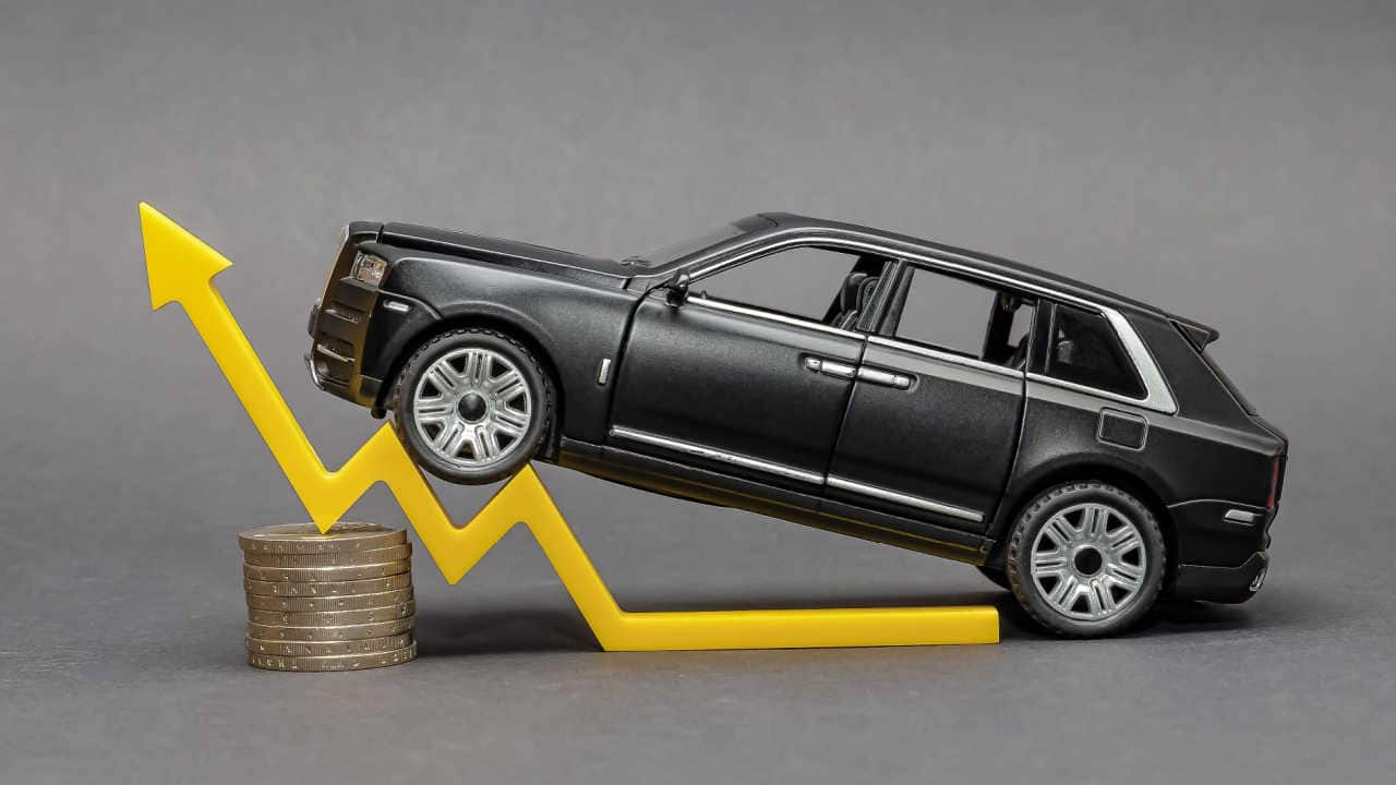 Miniatura de carro em cima de seta apontando para cima (em formato de gráfico) e de moedas empilhadas