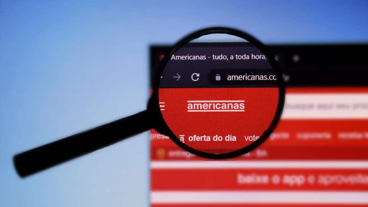 Lupa posicionada sobre o logo da Americanas em uma tela que mostra o site da empresa