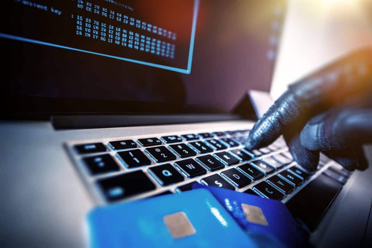 Mão de uma pessoa de luva utilizando computador. Sobre o teclado, dois cartões de crédito.