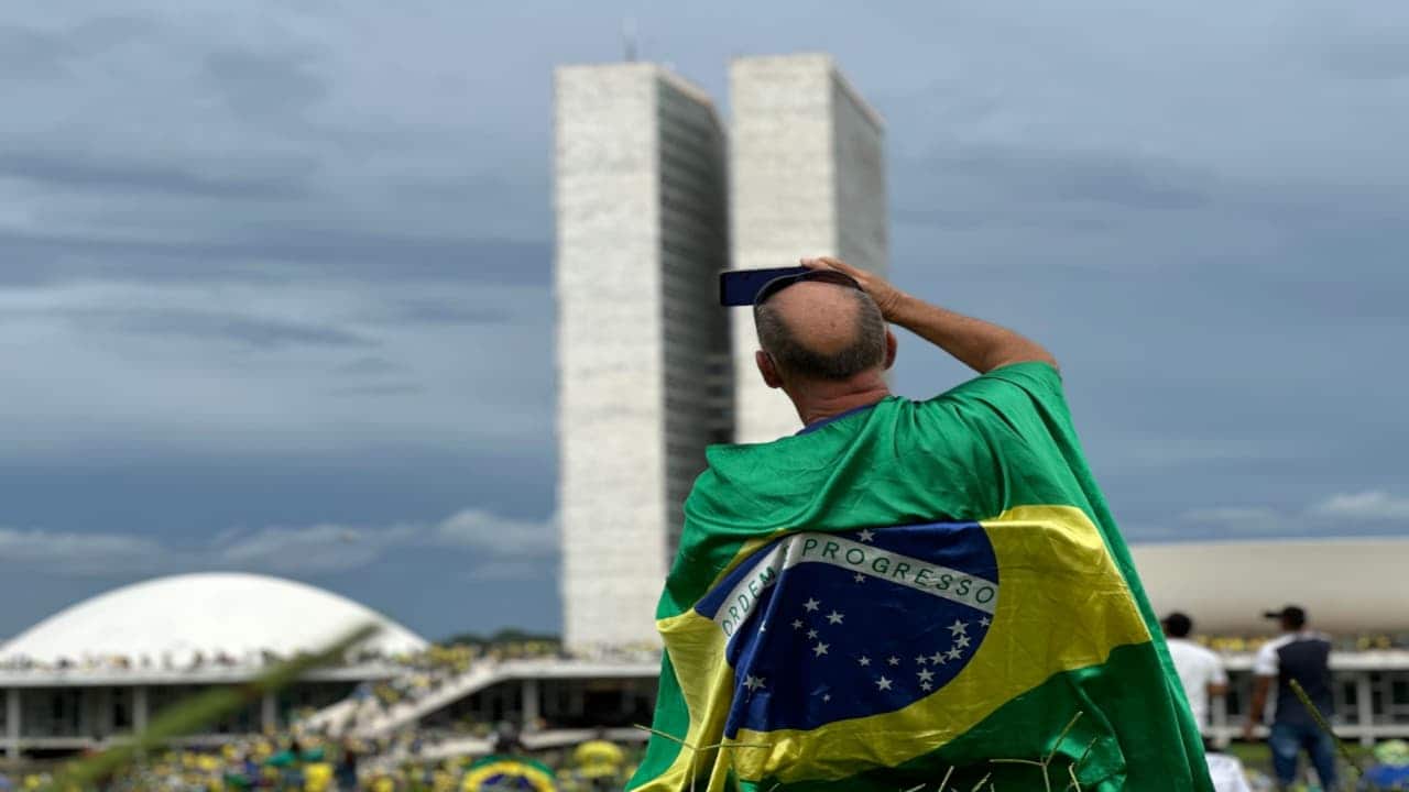 Homem enrolado em uma bandeira do Brasil filma pessoas invadindo Congresso Nacional