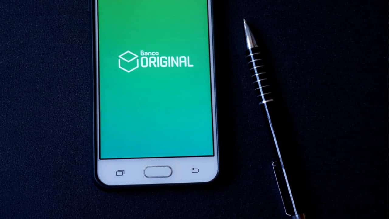 Posicionado ao lado de uma caneta, celular exibe aplicativo do Banco Original