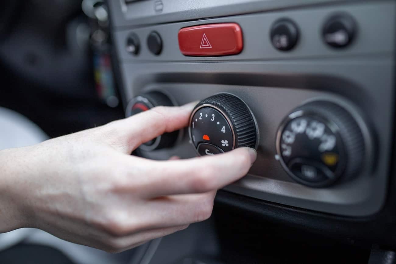 Mão de mulher mechendo no botão de ar condicionado do carro