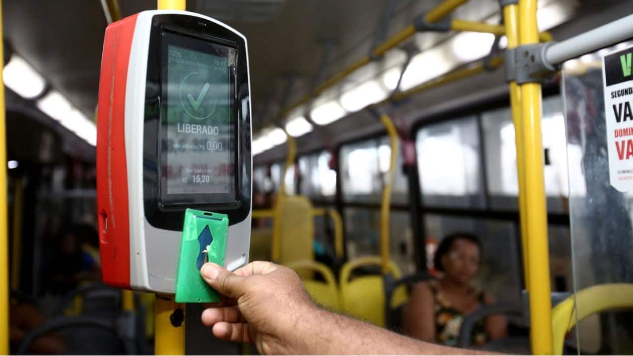 Mão de uma pessoa aproximando cartão da catraca de um ônibus e liberando a passagem