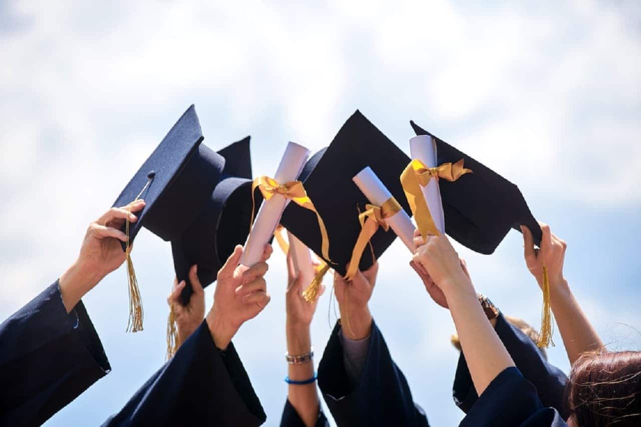 Imagem de pessoas levantando vários capelos de formatura.