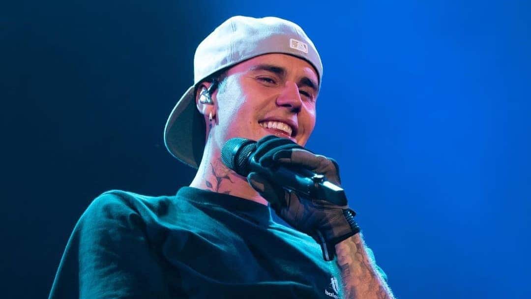 Cantor Justin Bieber sorrindo em show com microfone na mão