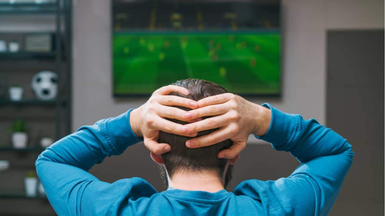 torcedor de costas, preocupado, enquanto assiste uma partida pela televisão