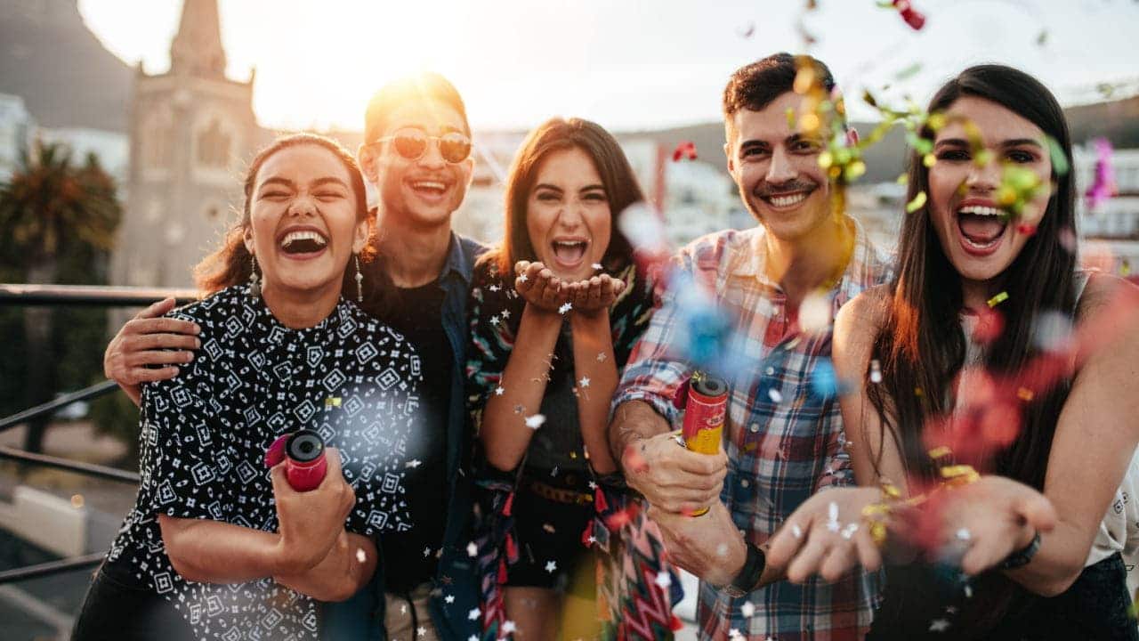 Grupo de cinco amigos sorrindo e lançando confete durante uma festa