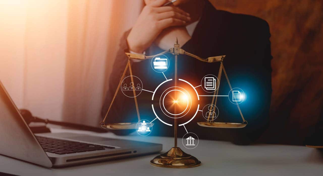Pessoa sentada a uma mesa com um notebook aberto à sua frente. Em primeiro plano, uma balança da justiça rodeada por ícones de arquivos e processos.