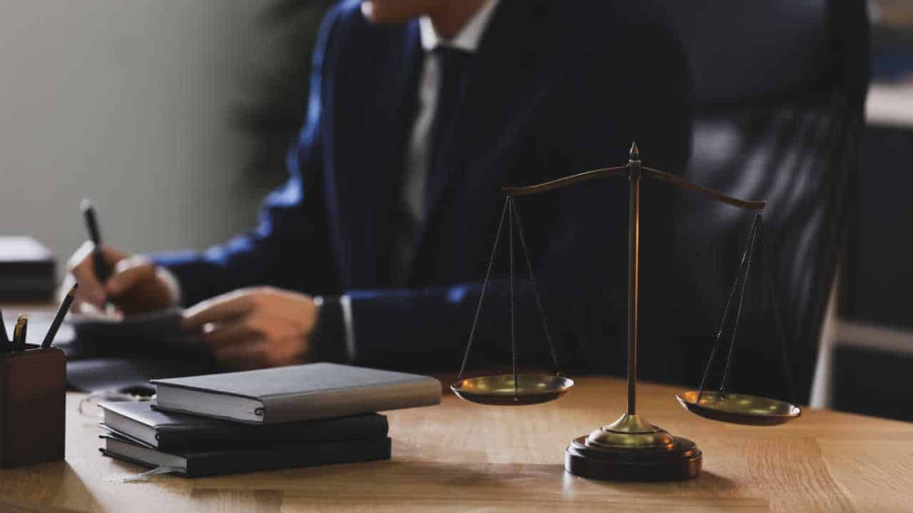advogado escrevendo com livros e balança da justiça sobre a mesa