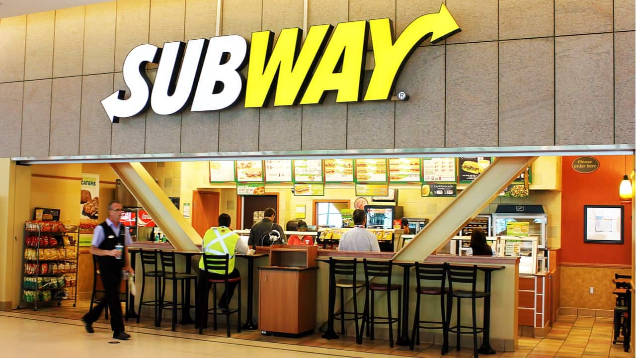 Foto da frente de um restaurante do Subway com duas pessoas aguardando pedido