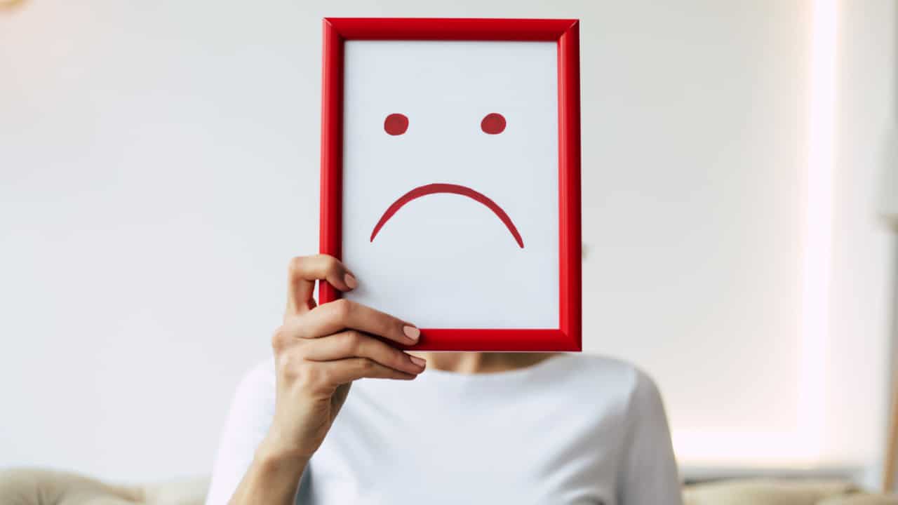Pessoa segurando, em frente ao seu rosto, um quadro com uma ilustração de expressão triste