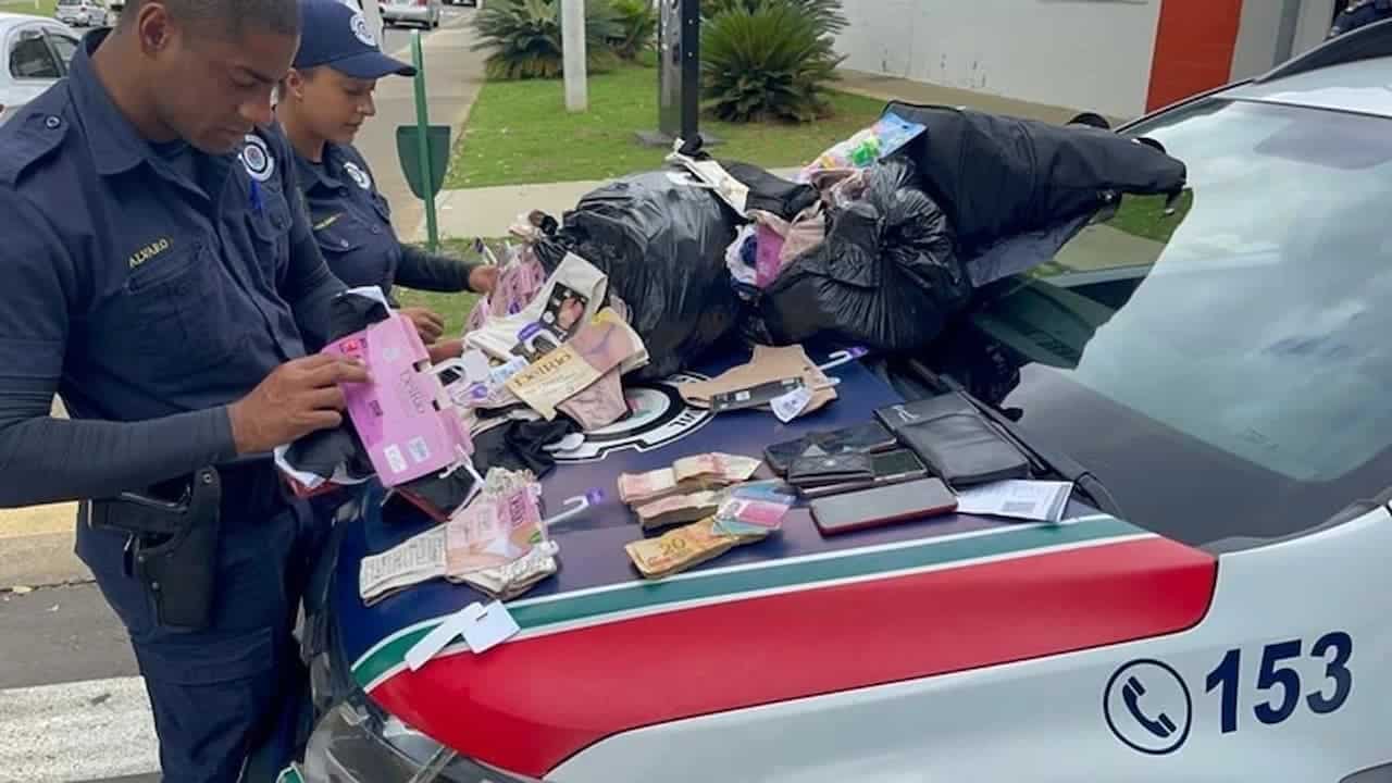 Policiais parados em frente a um capô de uma viatura onde calcinhas e celulares foram colocados