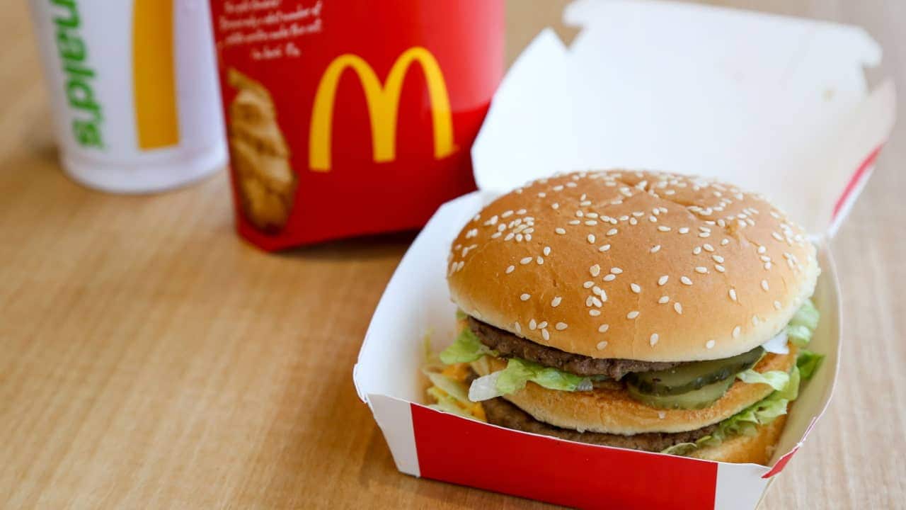 Combo de lanche da rede McDonald's, com hambúrguer à frente, batata e refrigerante ao fundo.