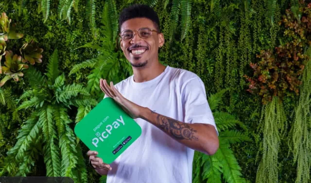 Moço segurando o logo do PicPay, com um fundo cheio de plantas