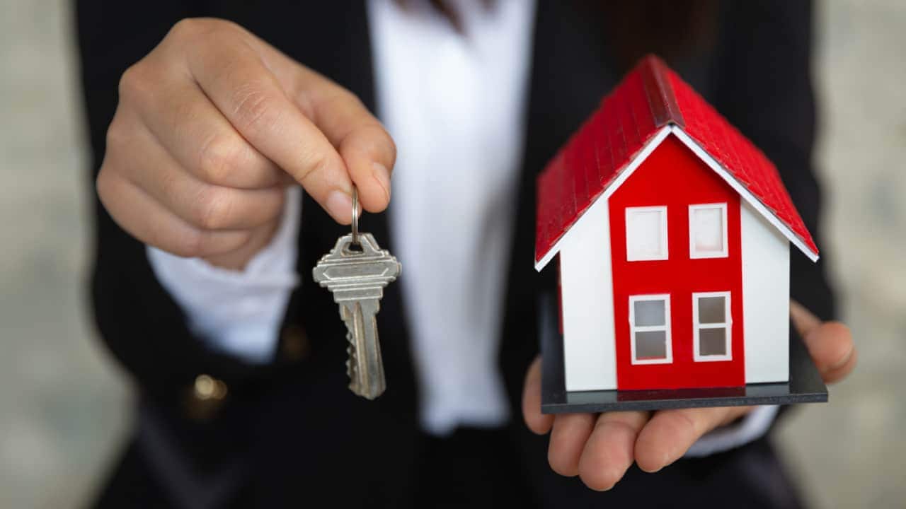 Mãos de uma pessoa segurando miniatura de um imóvel residencial e uma chave cpf