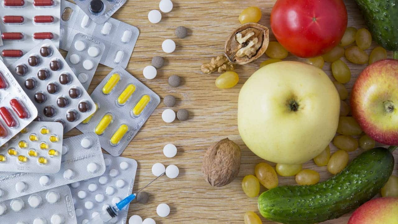 Mesa com várias cartelas de medicamentos, à esquerda, e várias frutas e legumes, à direita