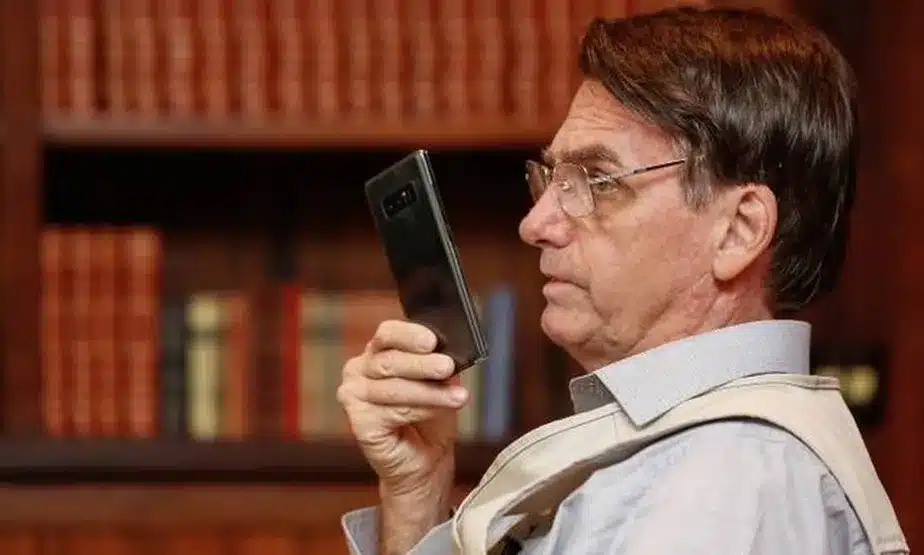 imagem mostra o ex presidente Bolsonaro com o celular na mão, sentado no escritório presidencial