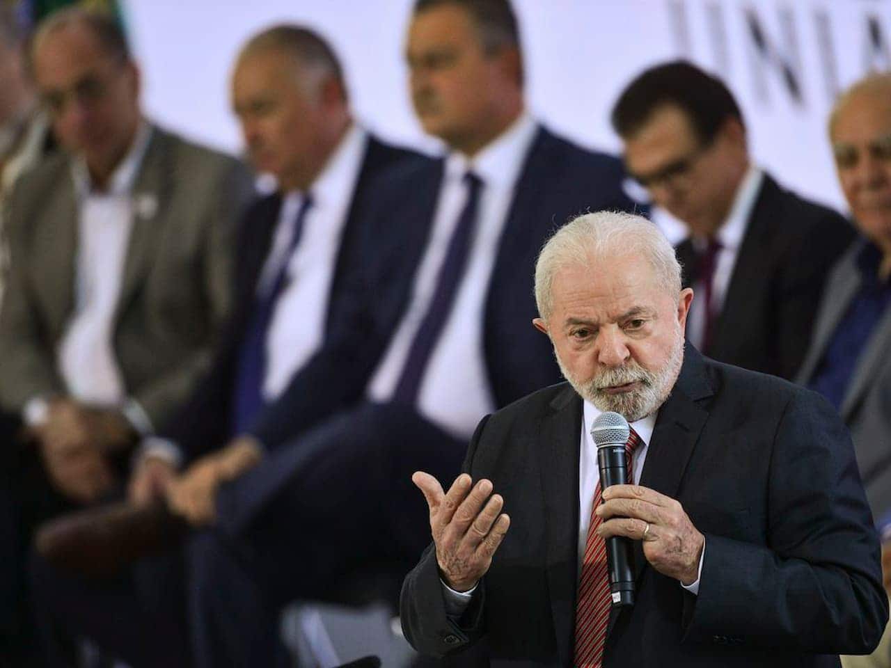 Lula em discurso com microfone na mão e pessoas ao fundo