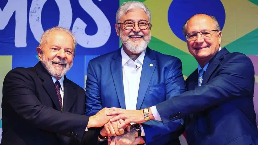 Presidente Lula, deputado Milton Coelho e vice-presidente Geraldo Alckmin sorrindo, com as mãos juntas em gesto de união