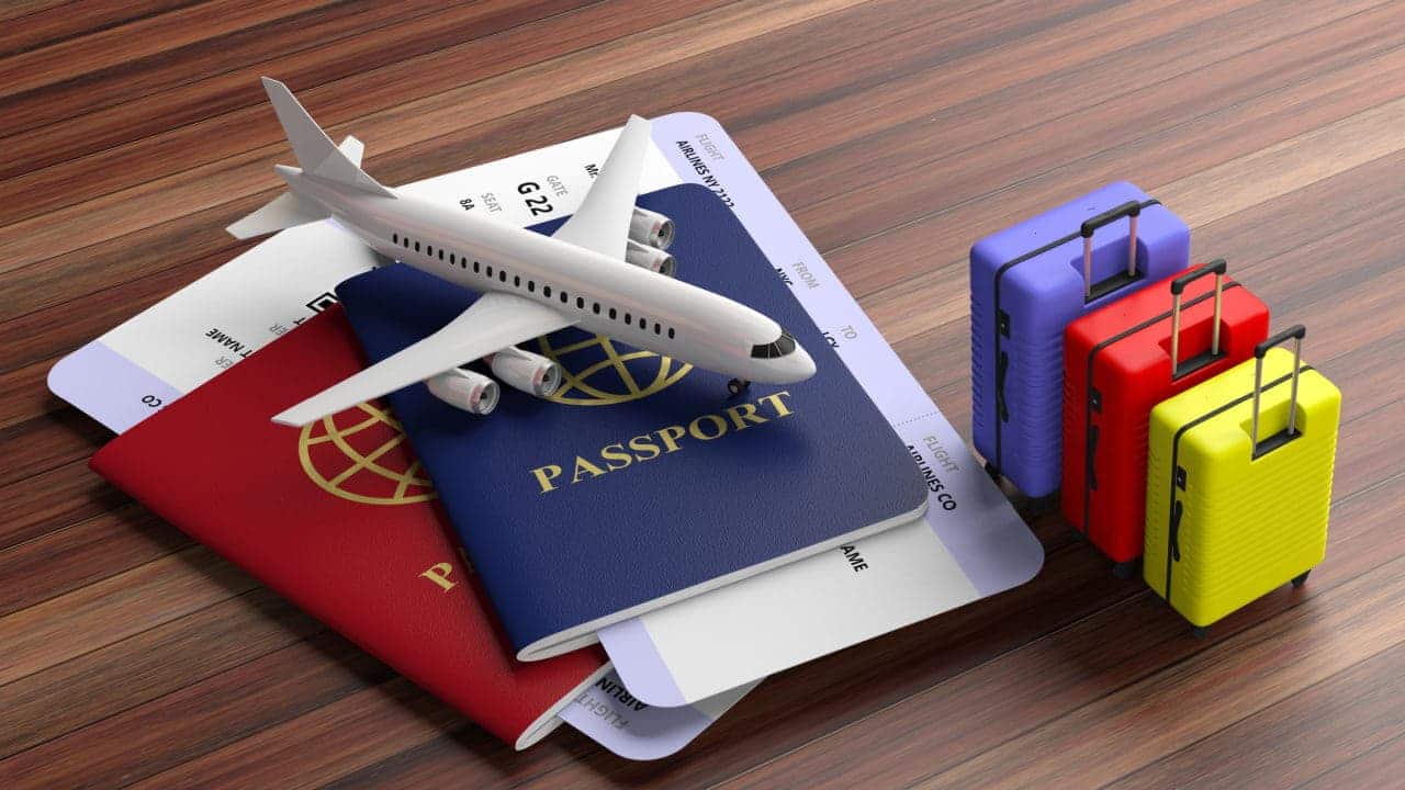 Miniatura de um avião sobre dois passaportes empilhados. Ao lado, três miniaturas de malas de viagem.